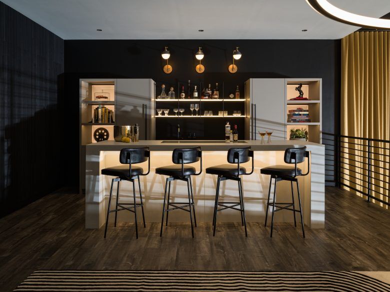 Bar u gornjem potkrovlju garaže s izloženim policama i četiri crne barske stolice.